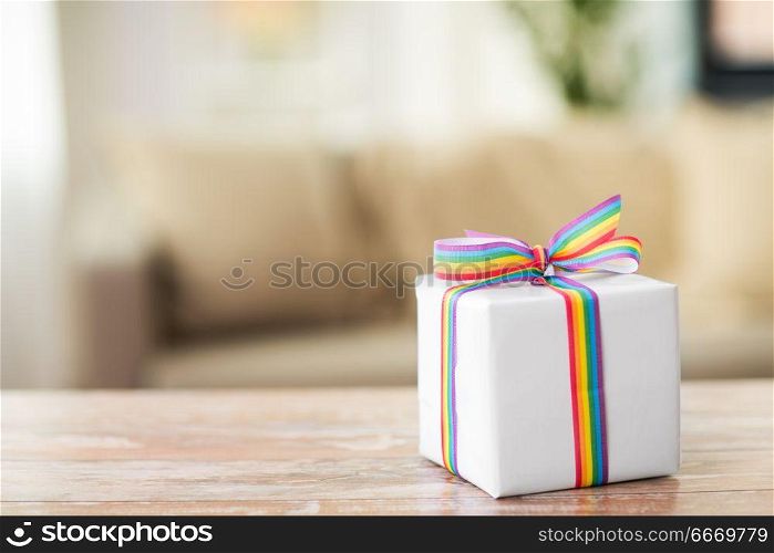homosexual and lgbt concept - gift box with gay pride awareness ribbon on wooden table at home. present with gay awareness ribbon on table at home. present with gay awareness ribbon on table at home