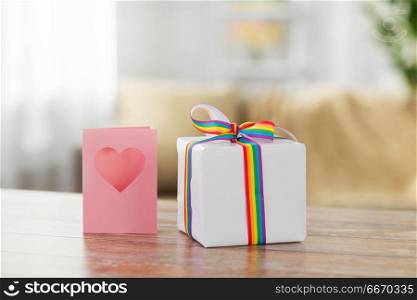 homosexual and lgbt concept - gift box with gay pride awareness ribbon and greeting card on wooden table at home. gift with gay awareness ribbon and greeting card. gift with gay awareness ribbon and greeting card