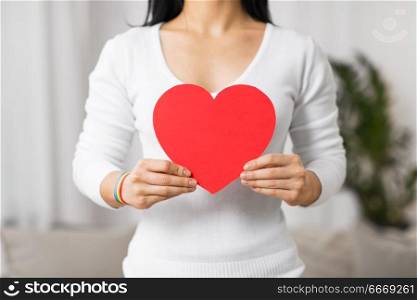 homosexual and lgbt concept - woman holding red heart shape and wearing gay pride awareness ribbon wristband. woman with gay awareness wristband holding heart. woman with gay awareness wristband holding heart