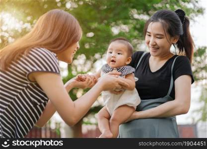 homosexual family of mothers hugs and plays with baby on a green bokeh background with sunlight