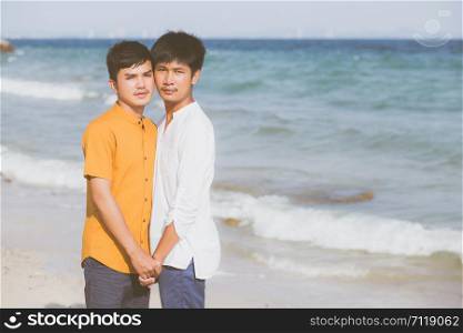 Homosexual portrait young asian couple standing together on beach in summer, asia gay holding hands going sea for leisure and relax with romantic and happy in vacation at sea, LGBT with legal concept.