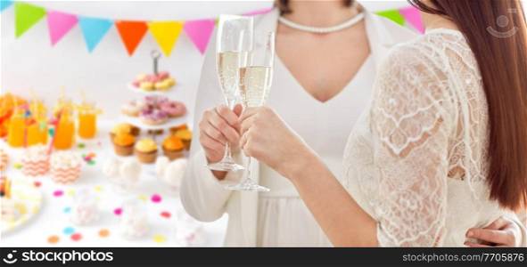 homosexuality, same-sex marriage and lgbt concept - close up of happy married lesbian couple hands holding and clinking champagne glasses over party background. close up of lesbian couple with champagne glasses