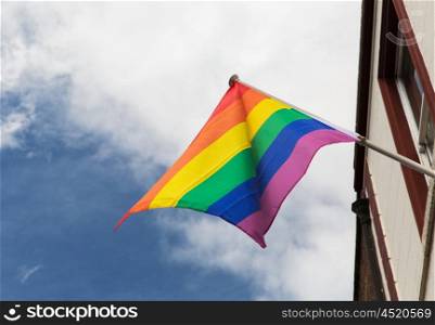 homosexuality, symbolics and gay pride concept - close up of rainbow flag waving on building