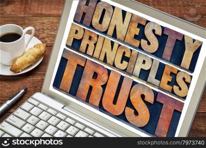 honesty, principles and trust concept - words in vintage letterpress wood type printing blocks stained by color inks on a laptop screen with a cup of coffee