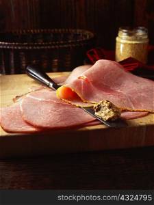 Honey and mustard ham slices with whole grain mustard, on wooden chopping board