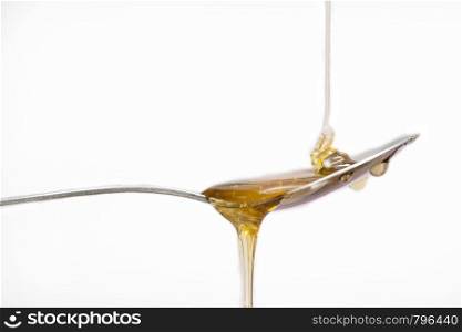 Honey dripping from a silver spoon on isolated white background food concept. Honey dripping from a silver spoon on isolated white background