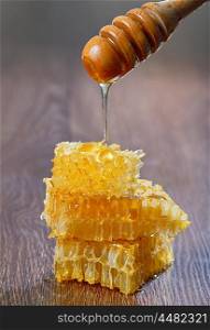 Honey dripping from a wooden drizzler over honeycomb