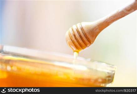 Honey dripping from a wooden honey dipper in a jar close up