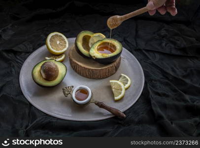 Honey dripping from wooden stick dripper into on Fresh organic avocado sliced in half and lemon sliced with honey on Ceramic tray. Healthy food concept, Selective Focus.