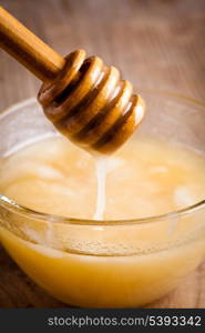 Honey dripping in glass bowl on wooden table