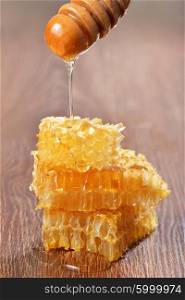 Honey dripping on honeycombs on wooden background