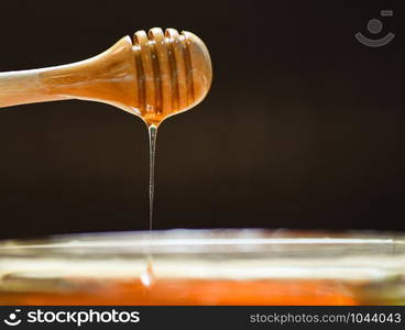 Honey dripping yellow sweet from wooden dipper honey on jar and dark background - selective focus