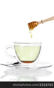 honey drops from a honey dipper in glass cup with green tea. honey drops from a honey dipper in glass cup with green tea on white background