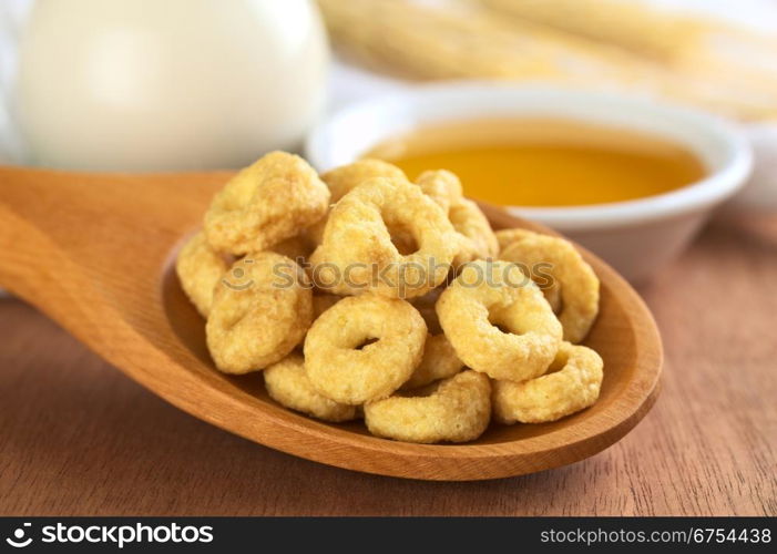 Honey flavoured cereal loops on wooden spoon with milk and honey in the back (Selective Focus, Focus on the front of the loops in the front). Honey Flavoured Cereal Loops