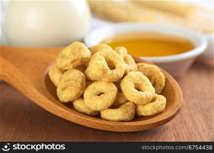 Honey flavoured cereal loops on wooden spoon with milk and honey in the back (Selective Focus, Focus on the front of the loops in the front). Honey Flavoured Cereal Loops