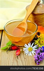 Honey in a glass bowl and a wooden pot, spoon, rosehip berries, flowers, napkin on the background of wooden boards