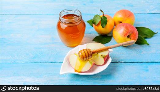 Honey jar and apple slices with honey on blue wooden background. Honey jar and apple slices with honey on blue wooden background. Rosh hashanah concept. Jewesh new year symbols. Copy space.