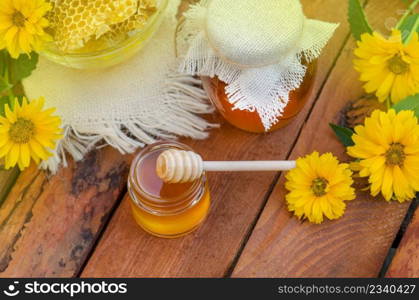 Honey jar and honeycomb on wooden table. Honey jar and flowes on table. Honey jar and wooden stick on table against green background