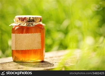 Honey jar with blank paper label on wooden table against green spring natural background