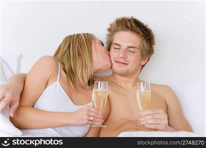 Honeymoon - young couple in bed kissing, drinking champagne