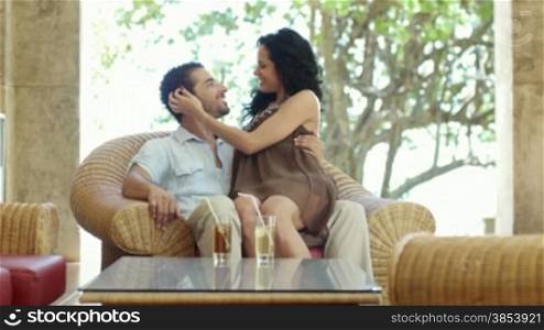 Honeymoon: young just married hispanic couple sitting on armchair in hotel bar and hugging