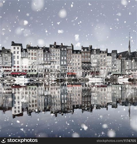 Honfleur harbour quay in Normandy, France in winter snowstorm. Magic famous snowy cityscape with houses reflection in the water. Christmas mood background. Monochromatic neutral tones, natural light