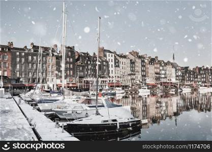 Honfleur harbour quay in Normandy, France in winter snowstorm. Magic famous snowy cityscape with houses reflection in the water. Christmas mood background. Monochromatic neutral tones, natural light