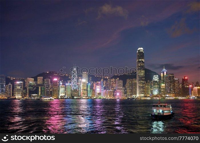 Hong Kong skyline cityscape downtown skyscrapers over Victoria Harbour in the evening illuminated with tourist boat ferries . Hong Kong, China. Hong Kong skyline. Hong Kong, China