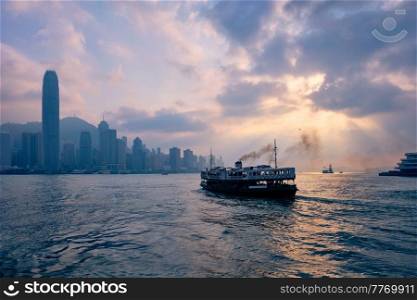 Hong Kong skyline cityscape downtown skyscrapers over Victoria Harbour on sunset with tourist ferry boat silhouette. Hong Kong, China. Hong Kong skyline. Hong Kong, China