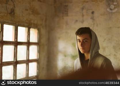 Hooded teenage boy in an abandoned house illuminated by a window