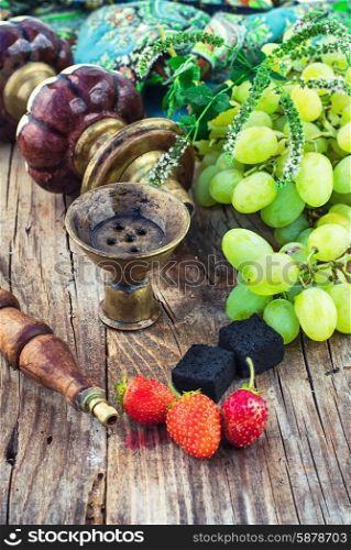 Hookah amid bunches of grapes and strawberries. Old smoking hookah and bunch of grapes on wooden surface.