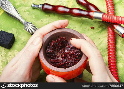 Hookah bowl with tobacco in the hands.Refueling tobacco shisha with fruit tobacco.Oriental smoking hookah.. Preparation of a smoking hookah