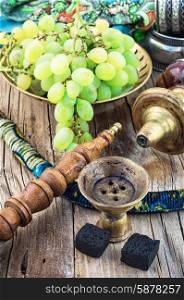 Hookah on wooden table. Old smoking hookah and bunch of grapes on wooden surface.