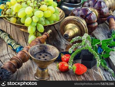 Hookah on wooden table. Old smoking hookah and bunch of grapes on wooden surface.
