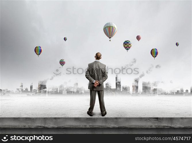 Hopeful businessman. Rear view of businessman looking at aerostats flying above city