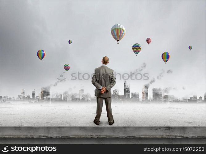 Hopeful businessman. Rear view of businessman looking at aerostats flying above city