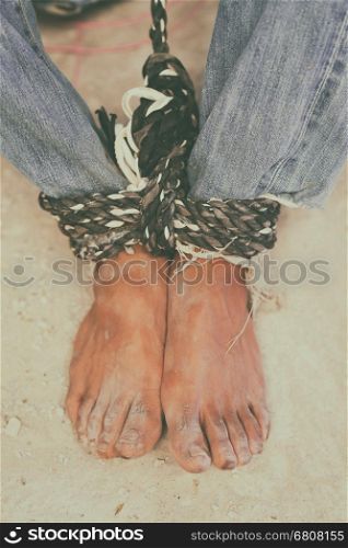 hopeless man feet tied together with rope, human trafficking