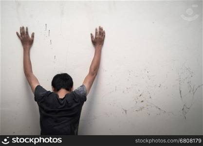 hopeless man show hands up facing the wall
