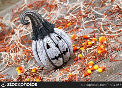 Horizontal angled image of a scary black and white pumpkin surround by shredded paper, candy and rustic wooden boards
