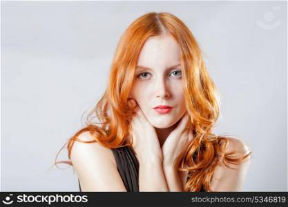 Horizontal beauty shot of a young blue eyed woman with her red hair, touching face by her hands, looks very shy