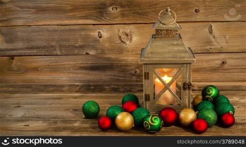 Horizontal front view of an old Asian design lantern and white candle glowing brightly inside with Christmas Ornaments on rustic wood