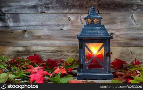 Horizontal image of a vintage metal lantern, candle burning inside, with autumn leaves and rustic wood on background
