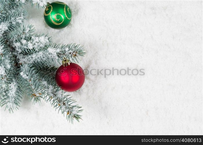 Horizontal image of Christmas ornaments, red and green, hanging from a real Blue Spruce tree branch placed on snow