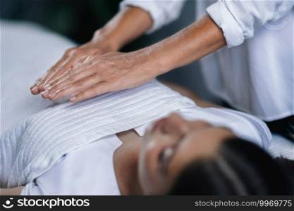 Horizontal image of female Reiki therapist holding hands over patient chest healing heart chakra. Peaceful beautiful teenage girl lying with her eyes closed.