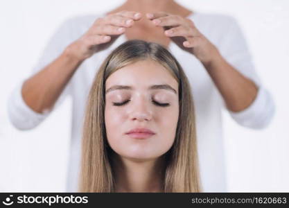 Horizontal image of female Reiki therapist standing and holding hands above head of the beautiful teenage patient. Reiki Practitioner transfers energy and healing crown chakra. Peaceful girl sitting with her eyes closed. Alternative therapy concept. 