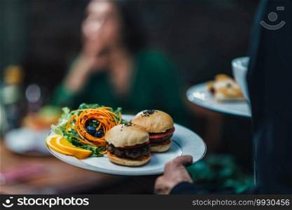 Horizontal image of male hand waiter serving plate of vegetarian burger dinner in restaurant to a beautiful young woman.