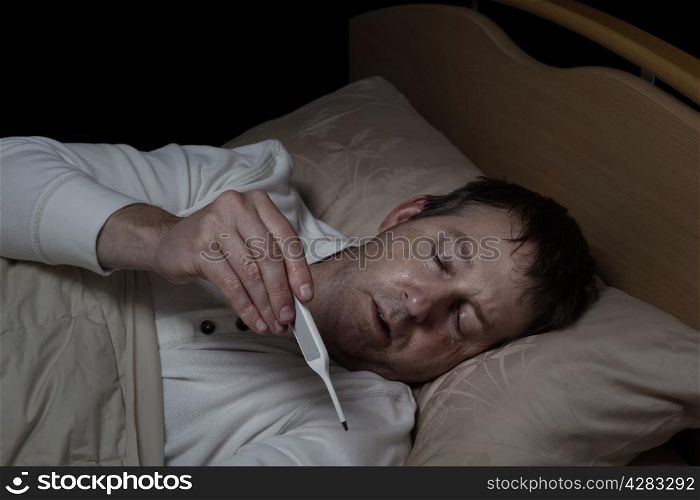 Horizontal image of mature man, reading thermometer, while lying down in bed
