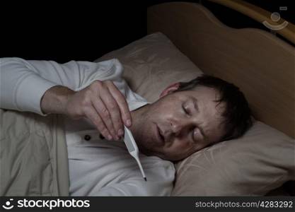 Horizontal image of mature man, reading thermometer, while lying down in bed