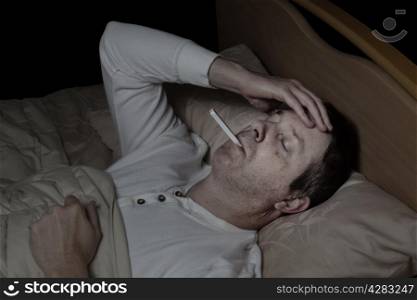 Horizontal image of mature man, with high fever, lying down in bed testing his temperature