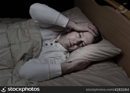Horizontal image of sick mature man, holding his head, while in bed